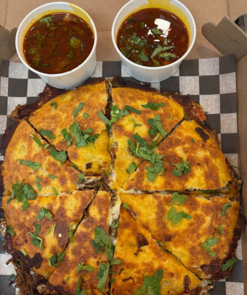 A freshly made birria quesadilla cut into slices, served with consommé for dipping
